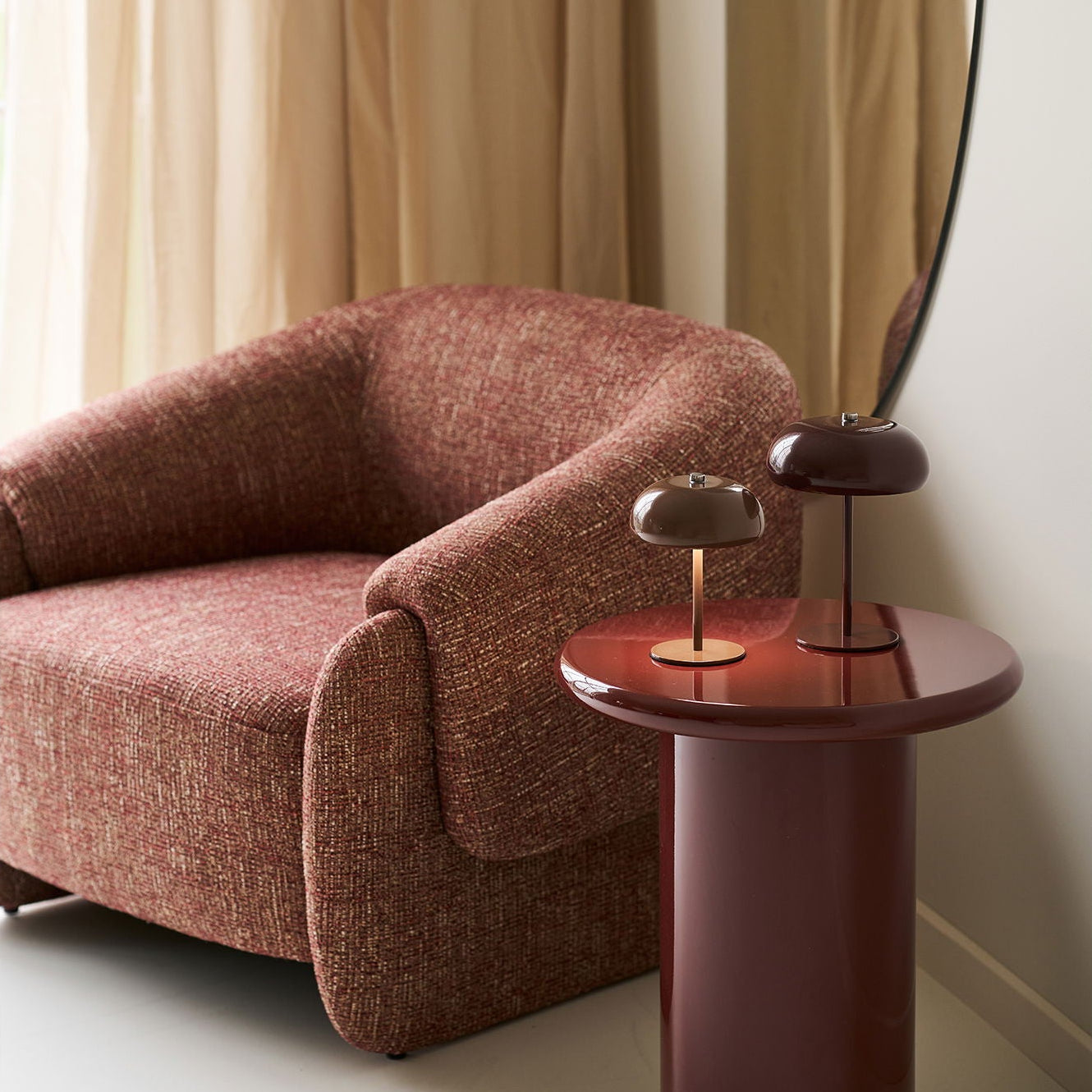 Brown armchair next to a matching side table with a lamp against a beige curtain.